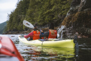 Two people kayaking along the coastline in British Columbia.